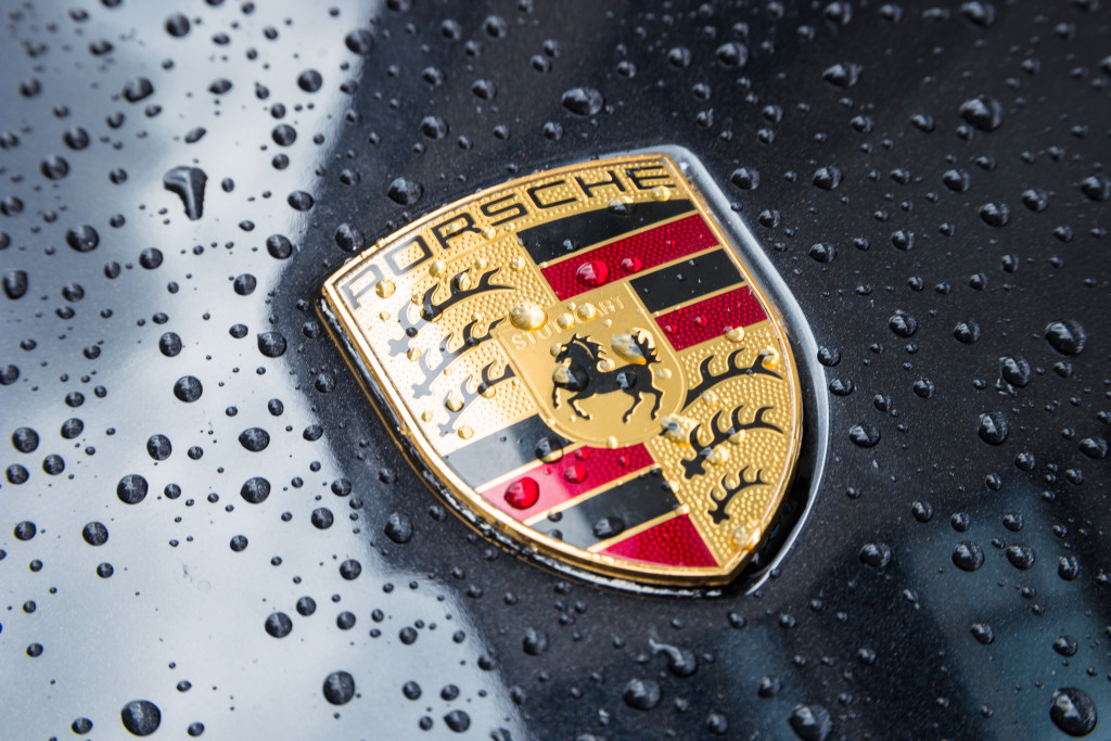 A close-up of the Porsche emblem on the hood of a car with droplets of water