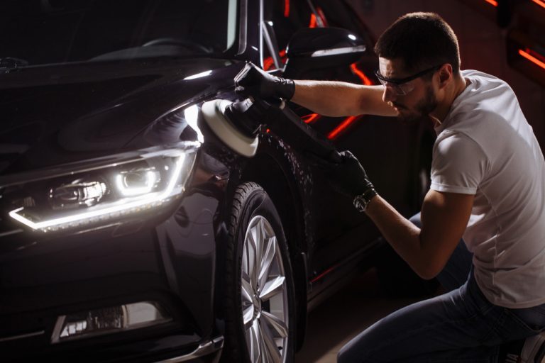 male mechanic wearing goggles white auto detailing a black car