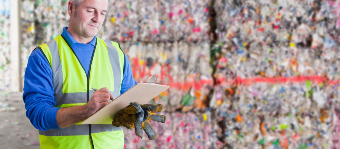 Male Worker With Clipboard Checking Waste Recycling Bales
