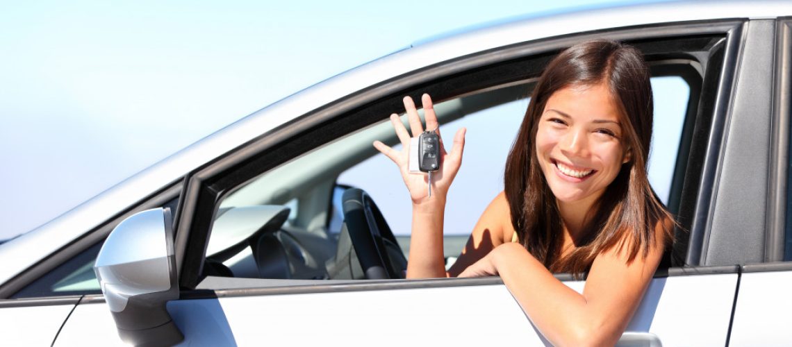 Teenage girl holding the keys to a car while sitting inside the vehicle.